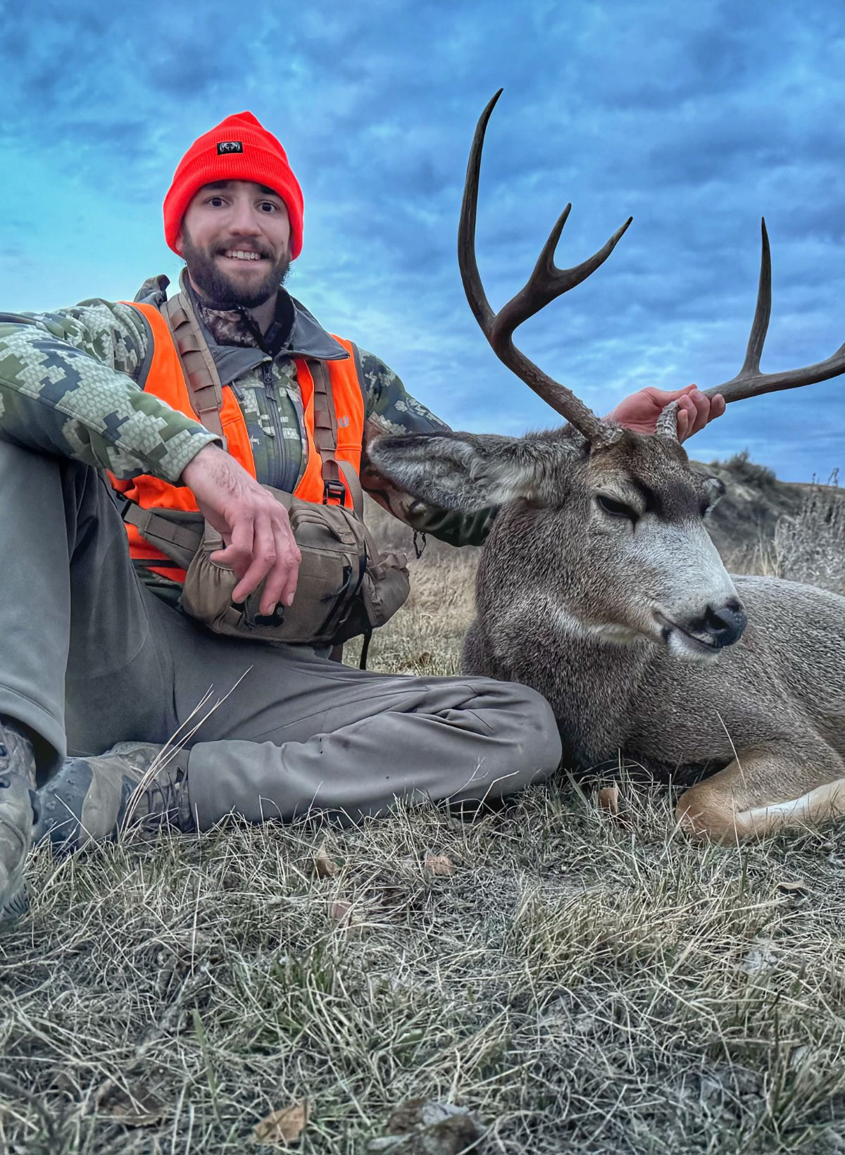 Hunter in NSG camouflage gear with a large deer on a grassy field